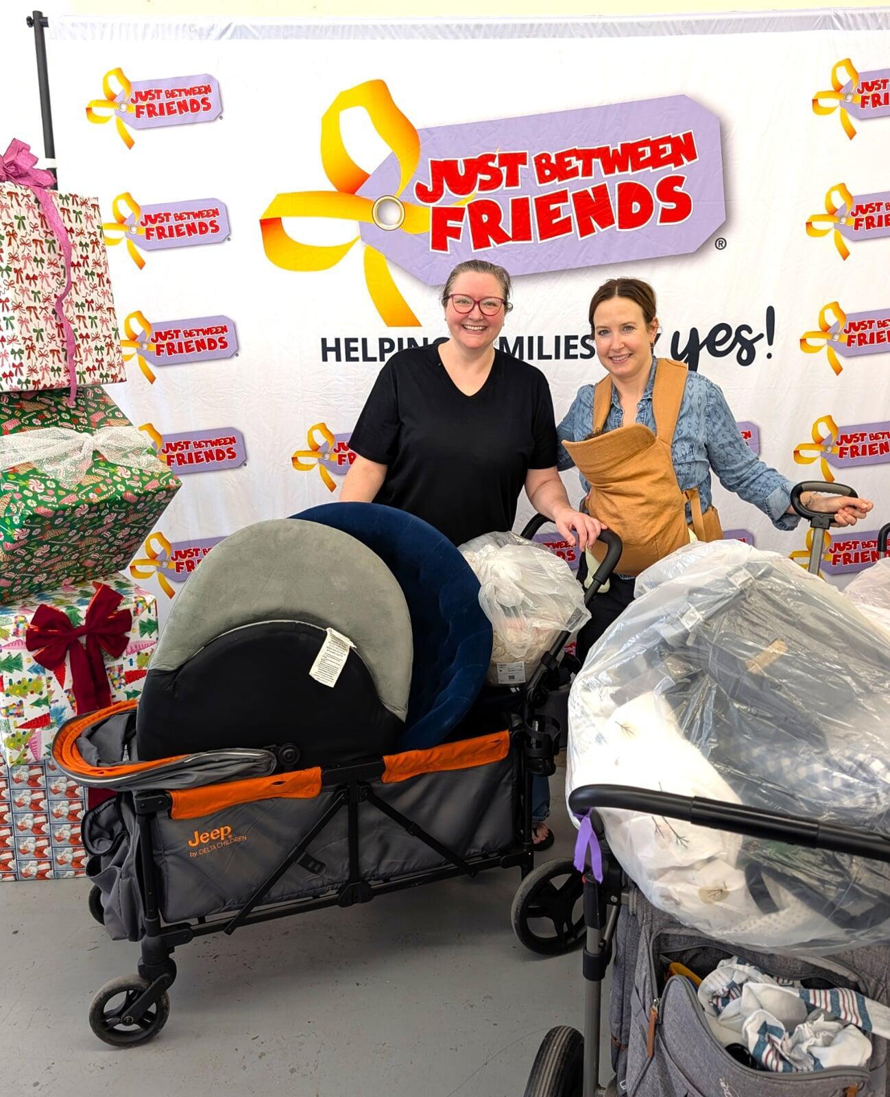 A woman kneels in front of racks of boys clothing. She is hold hangers full of boys clothing in both hands.