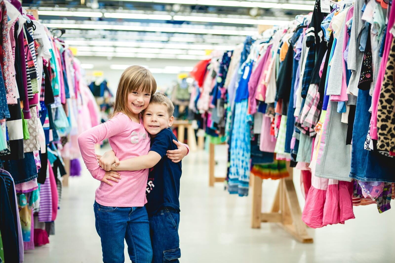 A mom and her four-year-old son stand with their masks and shopping bag in front of baskets of books and costumes.